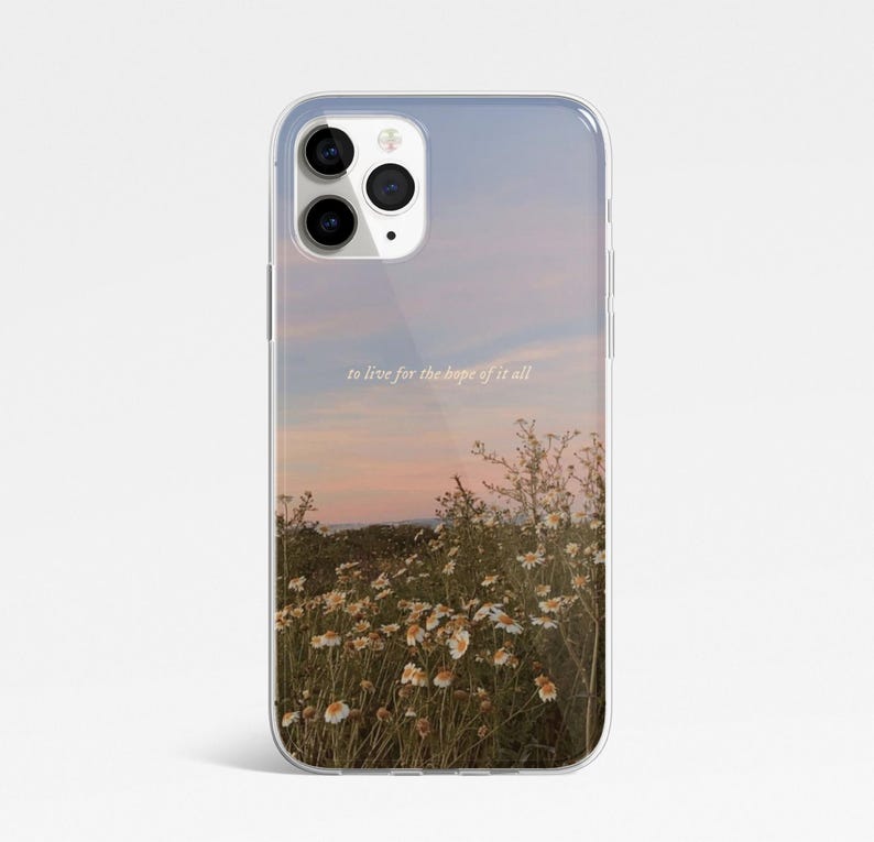 May include: Transparent phone case displaying a sunset scene with a field of white flowers. The text "to live for the hope of it all" is printed on the case. The case is designed to fit a smartphone.