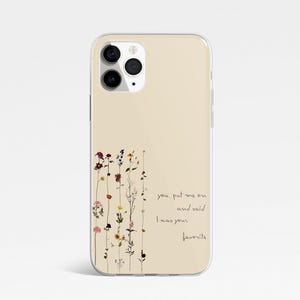 May include: A beige phone case featuring a floral design and the quote "you put me on and said I was your favourite." The case has a clear camera lens and a smooth finish. The floral design includes various colours.