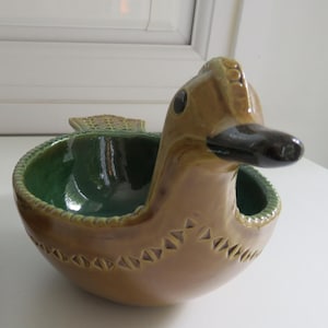 May include: Two ceramic duck-shaped bowls. The bowls are brown with green interiors and black beaks. The larger bowl is approximately 20 cm long, and the smaller bowl is about 13 cm long. The bowls have a decorative design around the base.