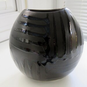Può includere: Un vaso in ceramica nera lucida, di forma arrotondata e con un'ampia apertura. Il vaso presenta un motivo strutturato e scanalato che avvolge l'esterno. Il colore scuro e la texture unica gli conferiscono un aspetto moderno e artistico.