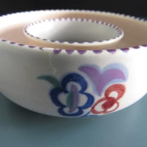 Könnte beinhalten: Weißer Keramikschale mit einer zentralen, kleineren Schale. Der Rand beider Schalen ist mit kleinen lila Punkten verziert. Blumendesigns in Blau, Lila, Rot und Grün zieren die Außenseite. Das Innere der Schalen ist hellrosa.