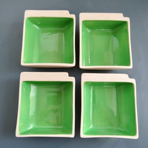 Könnte beinhalten: Vier quadratische Keramikschalen mit leuchtend grünem Innenraum und cremefarbenem Rand. Die Schalen haben ein einzigartiges Kerbdesign auf einer Seite. Die Schalen sind auf grauem Hintergrund quadratisch angeordnet.