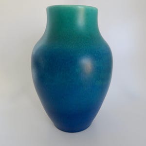 Könnte beinhalten: Eine hohe Keramikvase mit Farbverlauf. Die Oberseite der Vase ist türkisgrün und geht am Boden in ein tiefes Blau über. Die Vase hat eine glatte, abgerundete Form, geeignet für die Inneneinrichtung.