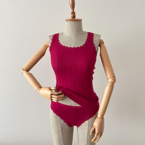 May include: A pink tank top and matching underwear with lace trim. The tank top has a scoop neck and the underwear has a low rise.