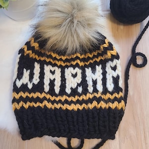 May include: Black knit beanie with a white pom pom and the word "WARM" knitted in white on a yellow stripe.