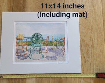 May include: A watercolor painting of five colorful chairs on a patio. The chairs are painted in shades of blue, green, yellow, and orange. The painting is matted and framed, measuring 11x14 inches.