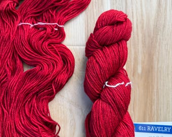 May include: Bright red yarn skeins and bundles. One bundle is neatly wound, while the other is loose and flowing. A label with the text "611 RAVELRY RIOS" is visible.