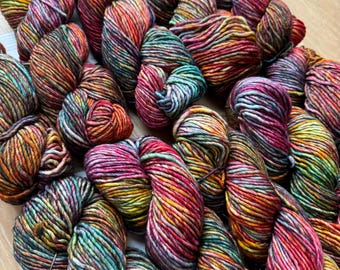 Puede incluir: Una colección de madejas de hilo coloridas de varios tamaños. El hilo muestra una vibrante mezcla de colores, incluyendo rojo, naranja, amarillo, verde y morado. Las madejas están dispuestas en un montón, mostrando la textura y las variaciones de color de la fibra.