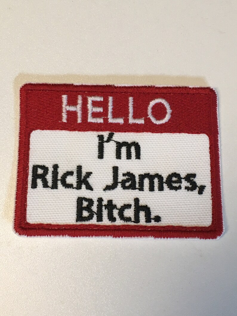 Peut inclure: Un &eacute;cusson rectangulaire avec une bordure rouge et un centre blanc. Le texte "HELLO" est en haut, avec "I'm Rick James, Bitch." en dessous en lettres noires. L'&eacute;cusson est probablement destin&eacute; aux v&ecirc;tements ou aux accessoires.