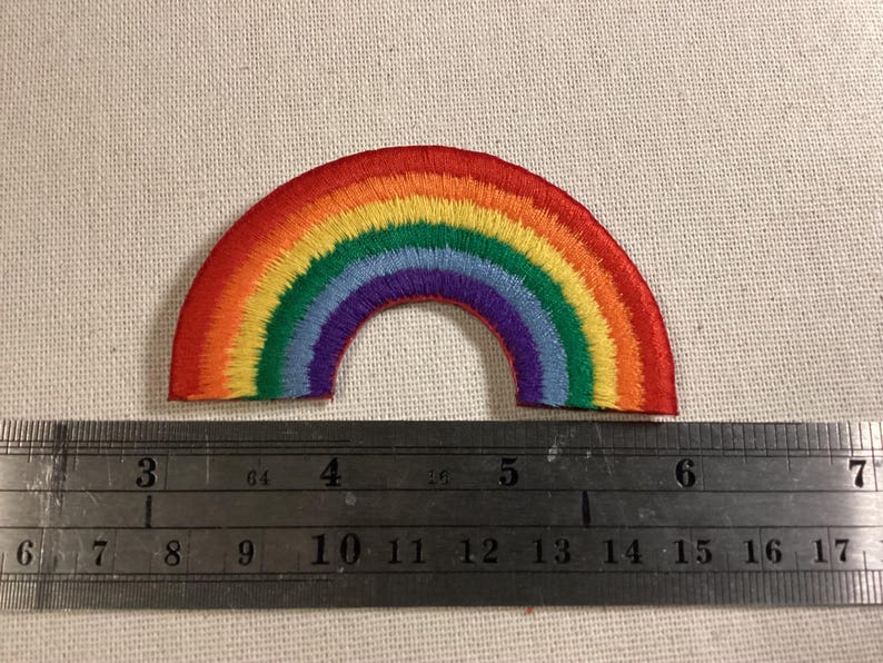 May include: A semi-circular rainbow embroidered patch featuring red, orange, yellow, green, blue, and purple thread. A metal ruler is positioned below the patch, showing it spans approximately 3.5 inches in width from end to end.