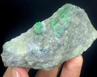 May include: A rough, gray rock with several bright green emerald crystals embedded in it.
