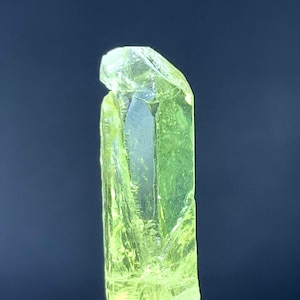 Puede incluir: Un cristal verde amarillo brillante con una textura clara y v&iacute;trea. El cristal est&aacute; sobre un soporte de exhibici&oacute;n de acr&iacute;lico transparente.