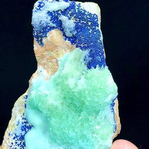 May include: A green and blue mineral specimen with a rough, textured surface. The specimen has a large, green, crystalline formation in the center, surrounded by a blue, crystalline formation.