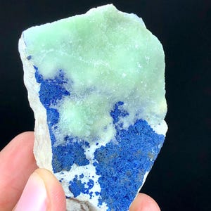 May include: A rough, light green and blue mineral specimen with a white matrix. The mineral has a crystalline structure and is a natural stone.