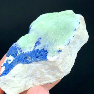 May include: A rough, natural rock specimen with a light green mineral on top and a dark blue mineral on the bottom.