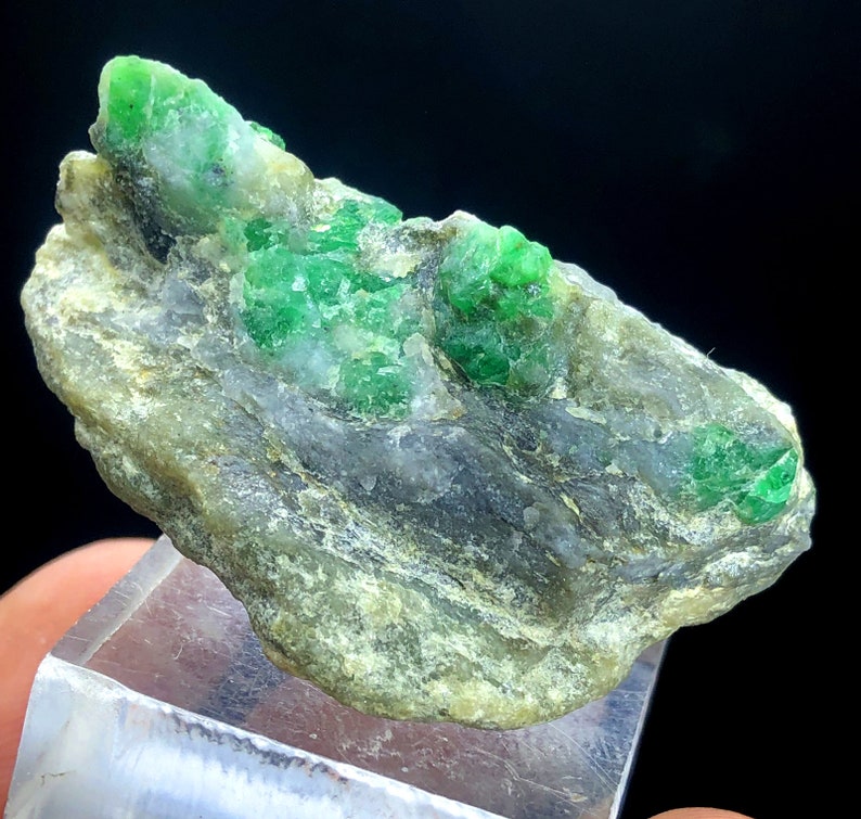 May include: A rough, gray rock with several bright green emerald crystals embedded in it.