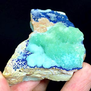 May include: A close-up of a blue and green mineral specimen. The specimen has a rough, textured surface and is composed of several different layers. The blue layer is on the top and bottom of the specimen, while the green layer is in the middle. The specimen is about 3 inches long and 2 inches wide.