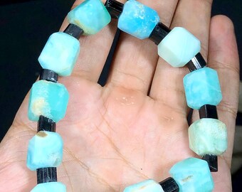 May include: A bracelet made of light blue and black beads. The blue beads are faceted and have a light blue and white color. The black beads are round and smooth.