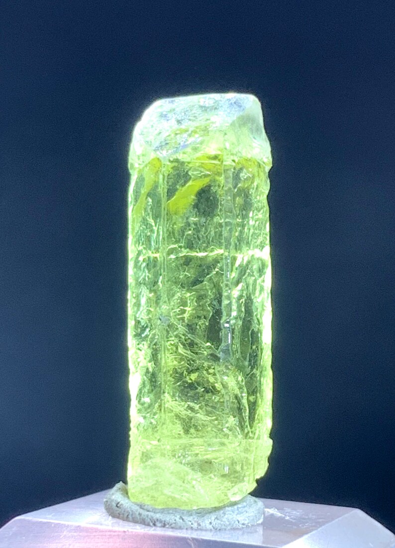 Puede incluir: Un cristal transl&uacute;cido verde brillante con una forma rectangular facetada. El cristal est&aacute; sobre una superficie blanca.