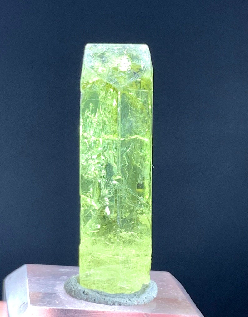 Puede incluir: Un cristal transl&uacute;cido verde brillante con forma rectangular. El cristal est&aacute; sobre una superficie gris.