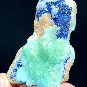 May include: A green and blue mineral specimen with a rough, natural texture. The specimen has a light green center surrounded by a darker blue border.