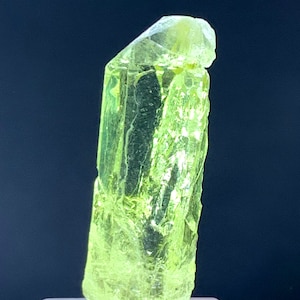 Puede incluir: Un gran cristal transl&uacute;cido verde brillante con una parte superior puntiaguda y una base plana. El cristal est&aacute; sentado sobre un pedestal blanco.