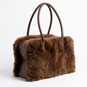 Peut inclure: Un sac &agrave; main marron de forme rectangulaire avec deux anses arqu&eacute;es. Le sac pr&eacute;sente un ext&eacute;rieur duveteux et textur&eacute; et une base en cuir marron. Une fermeture &eacute;clair dor&eacute;e traverse le dessus.