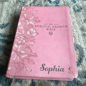 A pink Bible with the title "The Spiritual Growth Bible" and the name "Sophia" printed on the cover. The cover features a floral design in shades of pink and white.