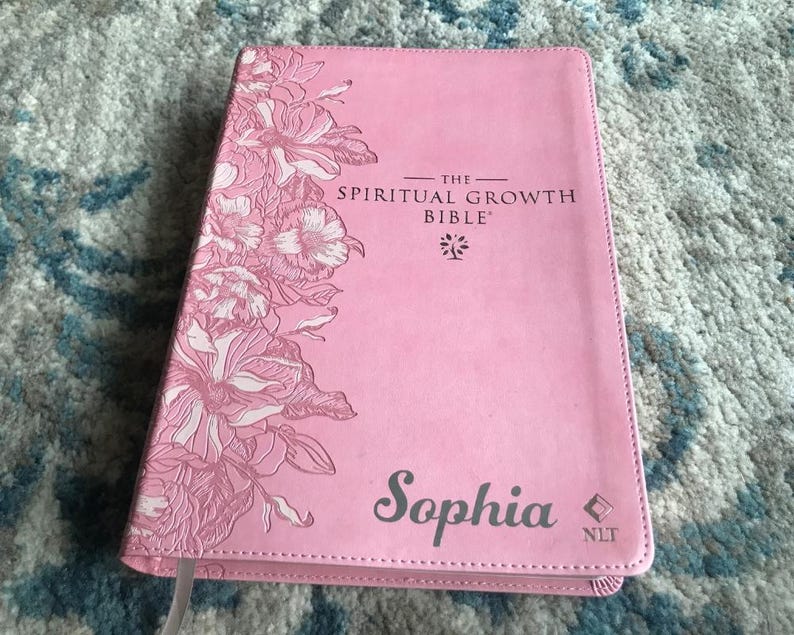 A pink Bible with the title "The Spiritual Growth Bible" and the name "Sophia" printed on the cover. The cover features a floral design in shades of pink and white.