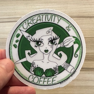May include: A circular sticker with a mermaid-style character, green eyes, and a seashell bra. The sticker features the words "CREATIVITY & COFFEE" in a green circle, with a paintbrush and coffee beans.