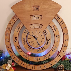 May include: A wooden perpetual calendar clock with a circular design. The clock face features Roman numerals and the days of the week in Italian. The calendar portion displays the months and dates in Italian. The clock is set to December 26th.