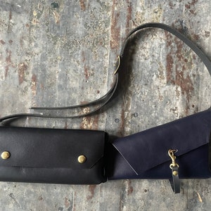 Puede incluir: Dos bolsos de bandolera de cuero, uno negro y otro azul oscuro, con herrajes dorados y correas ajustables.