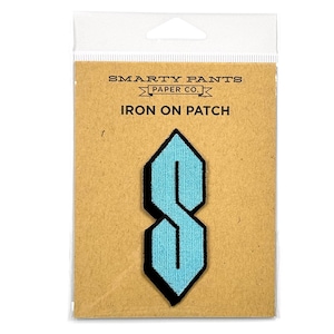 Op de afbeelding: Een lichtblauwe geborduurde strijkpatch in de vorm van een geometrische S, bevestigd op een beige kaart met het opschrift SMARTY PANTS PAPER CO. IRON ON PATCH. De patch heeft een scherp, hoekig ontwerp met een zwarte rand in een doorzichtige hoes.