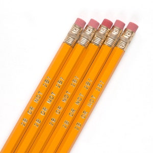 May include: Five yellow pencils with pink erasers and gold-colored metal bands. The pencils are printed with the text "2B OR NOT 2B?" in silver. The pencils are arranged diagonally against a white background.