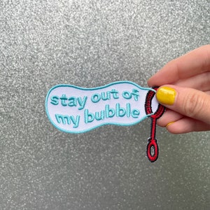 May include: A blue and white embroidered patch with the text "stay out of my bubble" and a red and black bubble wand.