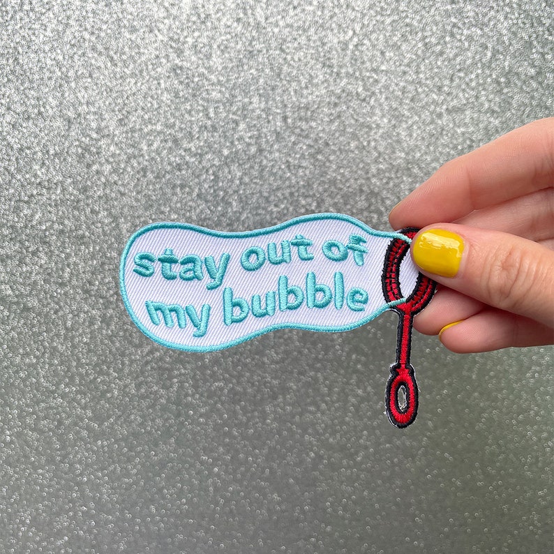 May include: A blue and white embroidered patch with the text "stay out of my bubble" and a red and black bubble wand.