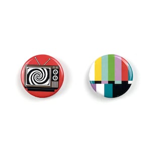 May include: Two round pinback buttons. One button is red with a black and white spiral television screen design. The other button has a colorful striped pattern of yellow, green, purple, and red. Both buttons are on a white background.