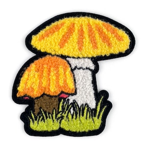 May include: Embroidered patch featuring two mushrooms with textured caps in yellow and orange, outlined in black. The mushrooms have white stems and sit atop green grass. A fun, whimsical design.