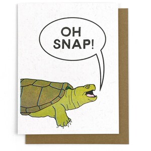 May include: Greeting card featuring a cartoon turtle with a green shell and a surprised expression. The turtle is speaking the words "OH SNAP!" in a speech bubble. The card is on a brown envelope.