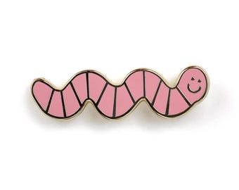 May include: A pink enamel pin shaped like a smiling worm with black outlines. The worm is segmented and has a happy face.