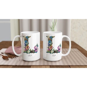 May include: Two white ceramic mugs with a floral design in the shape of the letter L. The mugs have the name "Lily" printed on the bottom.