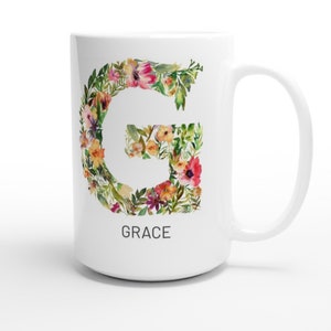 May include: White ceramic mug with a floral design in the shape of the letter G. The mug has a black handle and the word "GRACE" is printed below the design.
