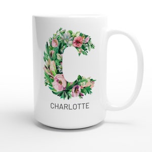 May include: White ceramic mug with a floral design in shades of pink and green. The design features the letter "C" surrounded by flowers and leaves. The name "CHARLOTTE" is printed below the design.