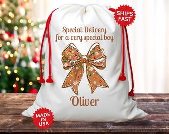 May include: White Christmas gift bag with red drawstring closure. The bag features a gingerbread bow design with the text "Special Delivery for a very special boy" and the name "Oliver".