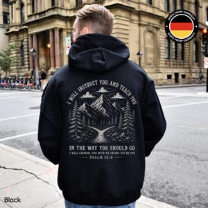 Könnte beinhalten: Schwarzer Kapuzenpullover mit Berg- und Waldgrafik auf dem Rücken, begleitet von dem Text "I WILL INSTRUCT YOU AND TEACH YOU" und "IN THE WAY YOU SHOULD GO". Der Hoodie ist schwarz und hat eine Kapuze.