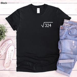 Op de afbeelding: Een zwart T-shirt met korte mouwen en een witte afbeelding op de linkerborst. De afbeelding toont een vierkantswortelsymbool gevolgd door het getal 324. Het T-shirt heeft een ronde hals en een standaard pasvorm op een plat oppervlak.