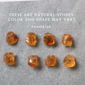 May include: Eight raw, natural stones with a translucent, amber color are arranged on a gray surface. The stones vary in shape and size. Text at the top reads: "THESE ARE NATURAL STONES. COLOR AND SHAPE MAY VARY. examples."