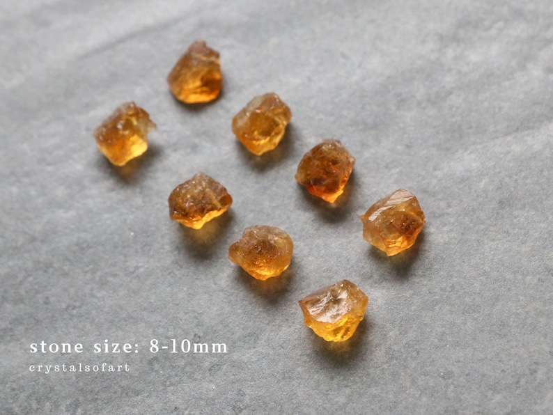 May include: Eight rough-cut citrine gemstones, each approximately 8-10mm in size, are scattered on a gray surface. The stones have a warm, amber color with variations in transparency and texture. The text "stone size: 8-10mm" is visible.