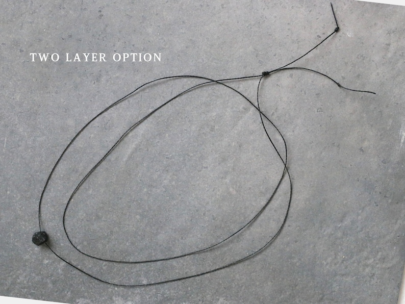 Puede incluir: Un collar negro con un dise&ntilde;o de dos capas. El collar presenta una peque&ntilde;a cuenta de color oscuro y se muestra sobre un fondo gris. El texto "TWO LAYER OPTION" es visible en la imagen.