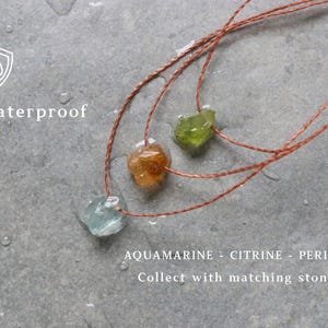 May include: Three gemstone necklaces featuring aquamarine, citrine, and peridot stones on brown cords. The image includes the text "Waterproof" and the names of the gemstones. The necklaces are displayed on a grey surface.